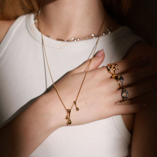 Person wearing a gold necklace and multiple rings on a neutral background