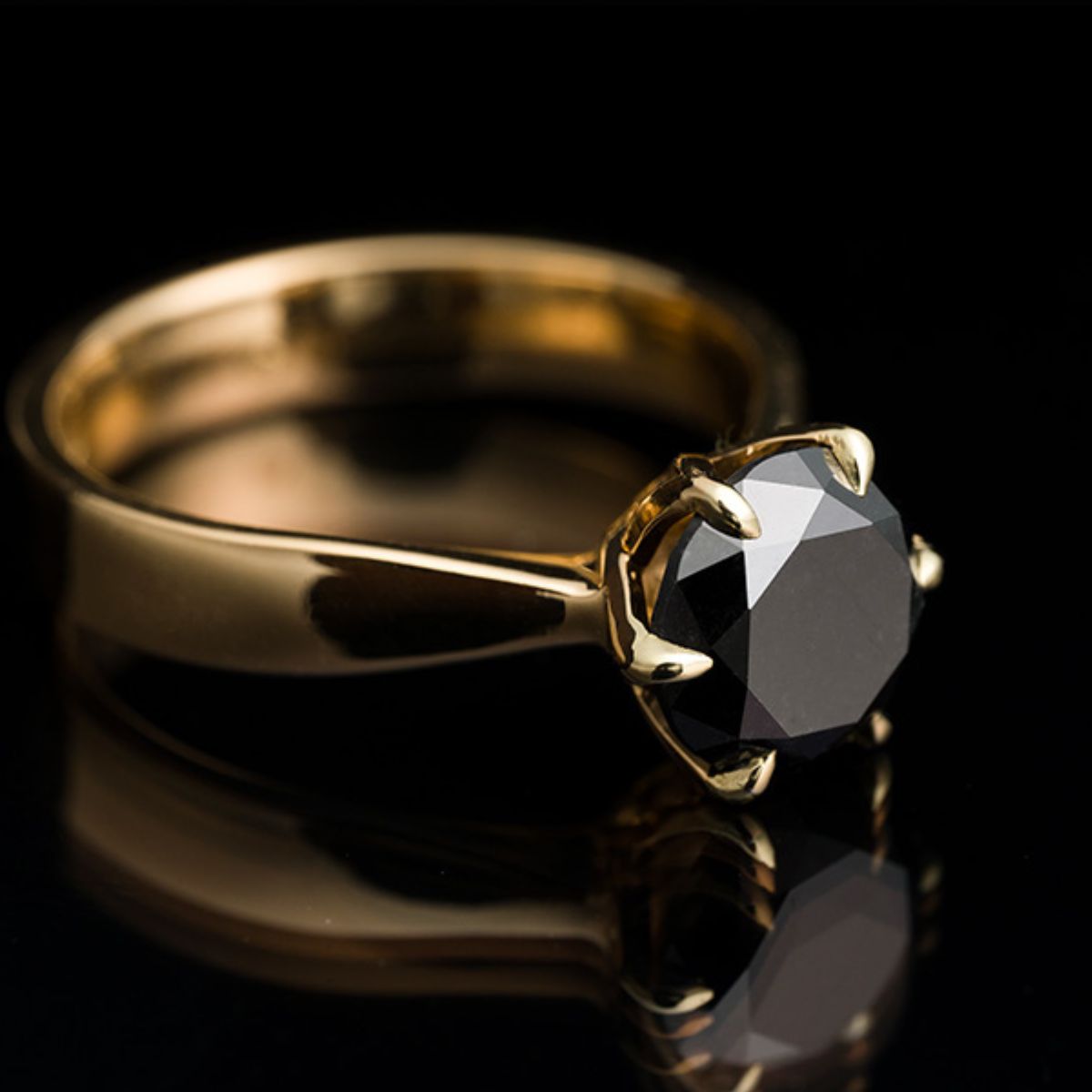 Gold ring with a black gemstone on a reflective surface with a black background