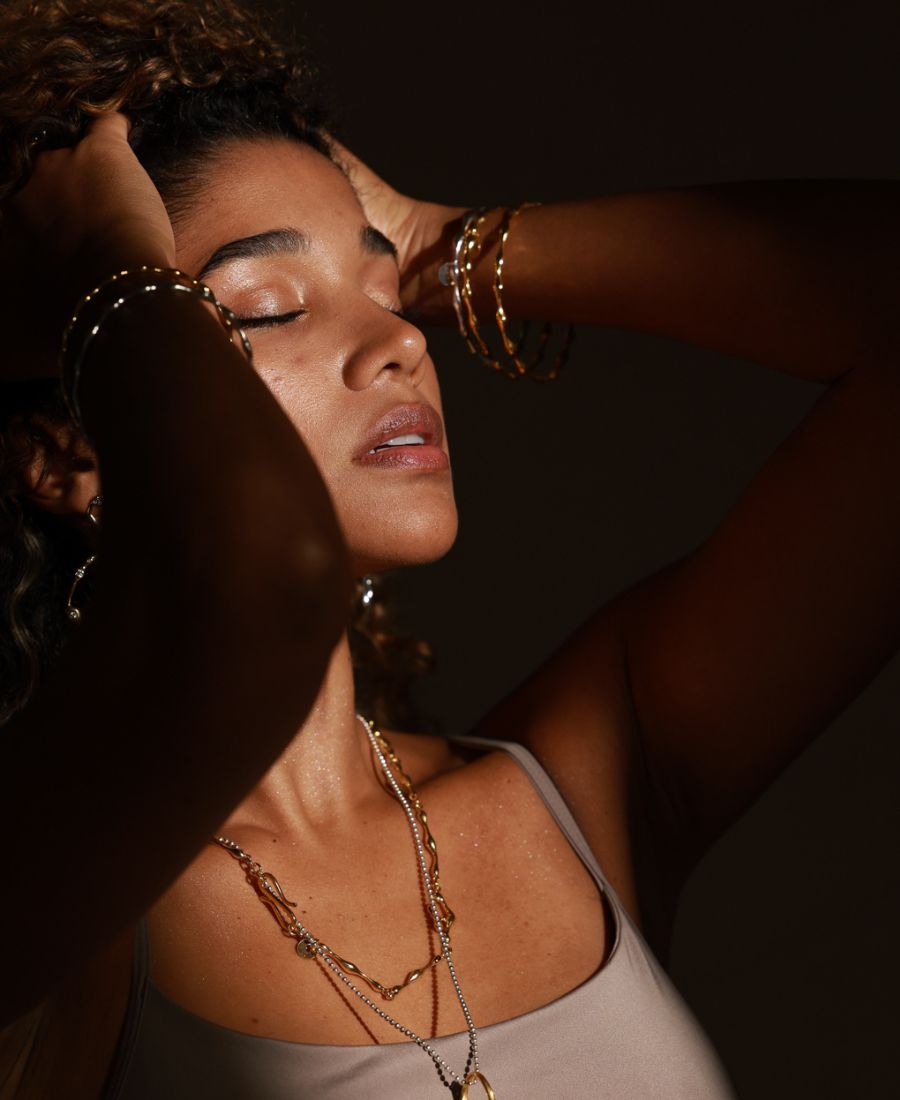 Woman with gold jewelry and necklaces against a dark background