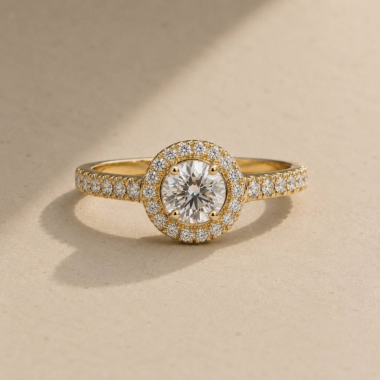 Yellow gold halo diamond engagement ring with pavé band on warm beige background