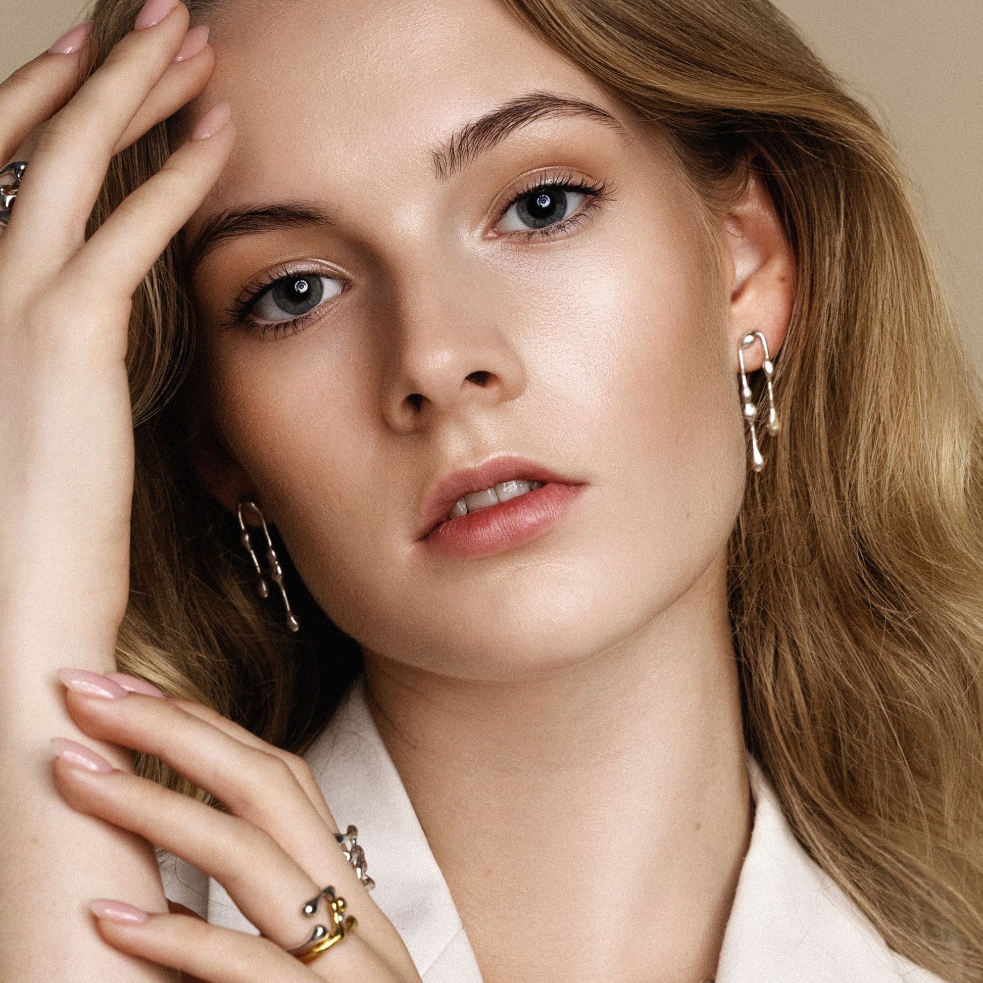 Close-up of a woman wearing gold earrings and rings with a neutral background