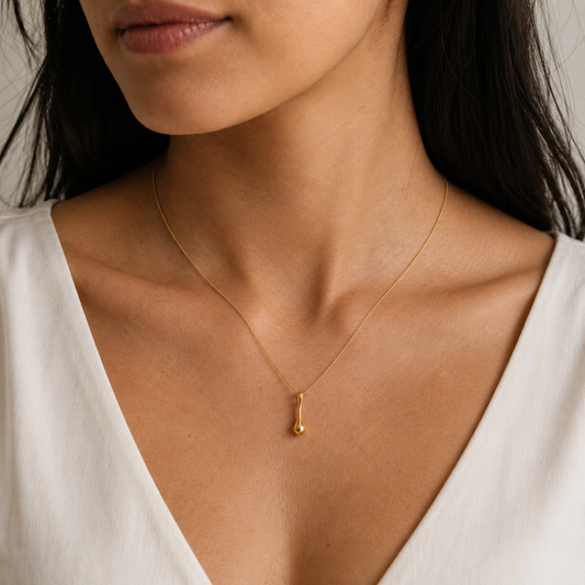 Close-up of a person wearing a gold necklace with a pendant against a neutral background