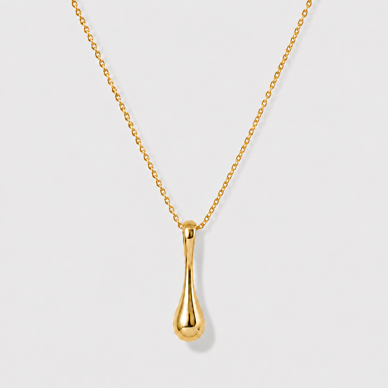 Minimal sculptural gold drop pendant necklace on delicate chain against soft neutral background