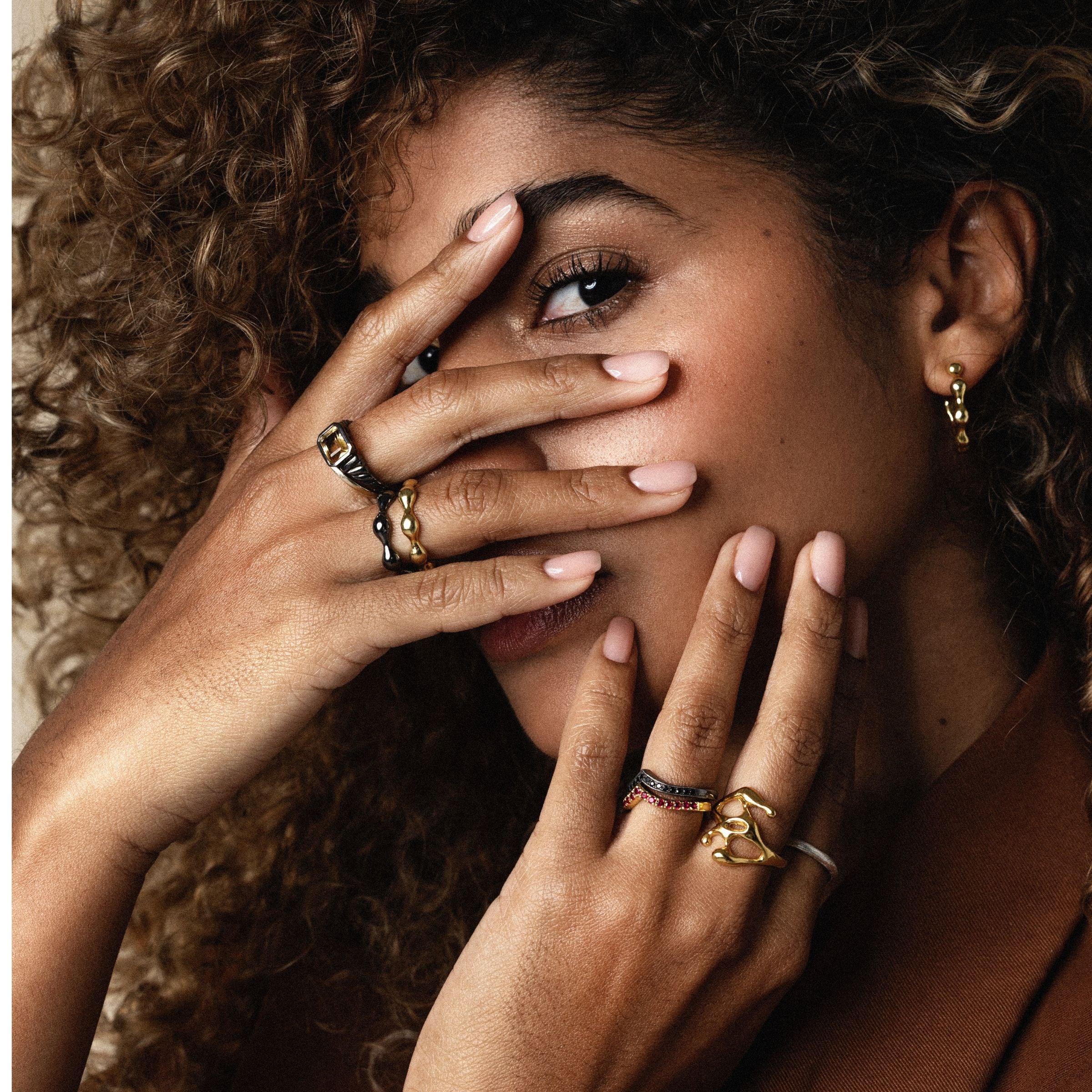 Woman with curly hair covering her face with her hands, wearing multiple rings by JYOCO including citrine signet ring and black diamonds ring 