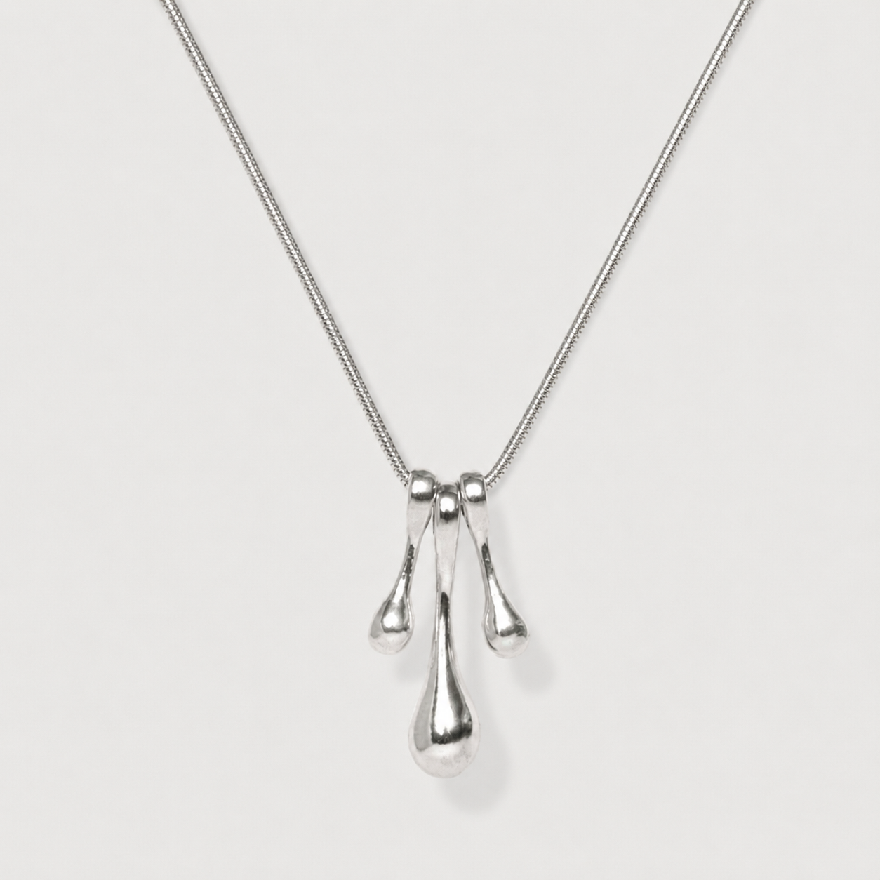 Silver necklace with three droplet pendants on a light gray background