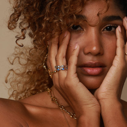 Woman with curly hair wearing gold jewelry against a neutral background