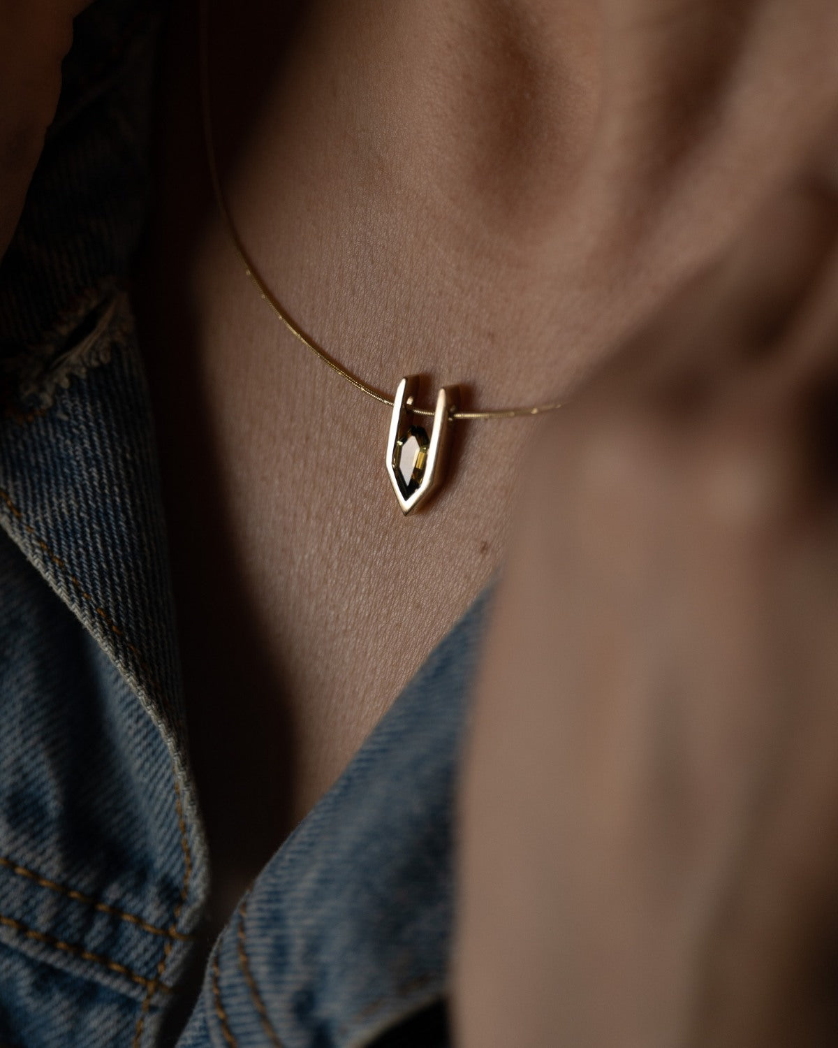 Gold and sapphire necklace made by JYOCO with a unique pendant worn by a person against a blurred background 
