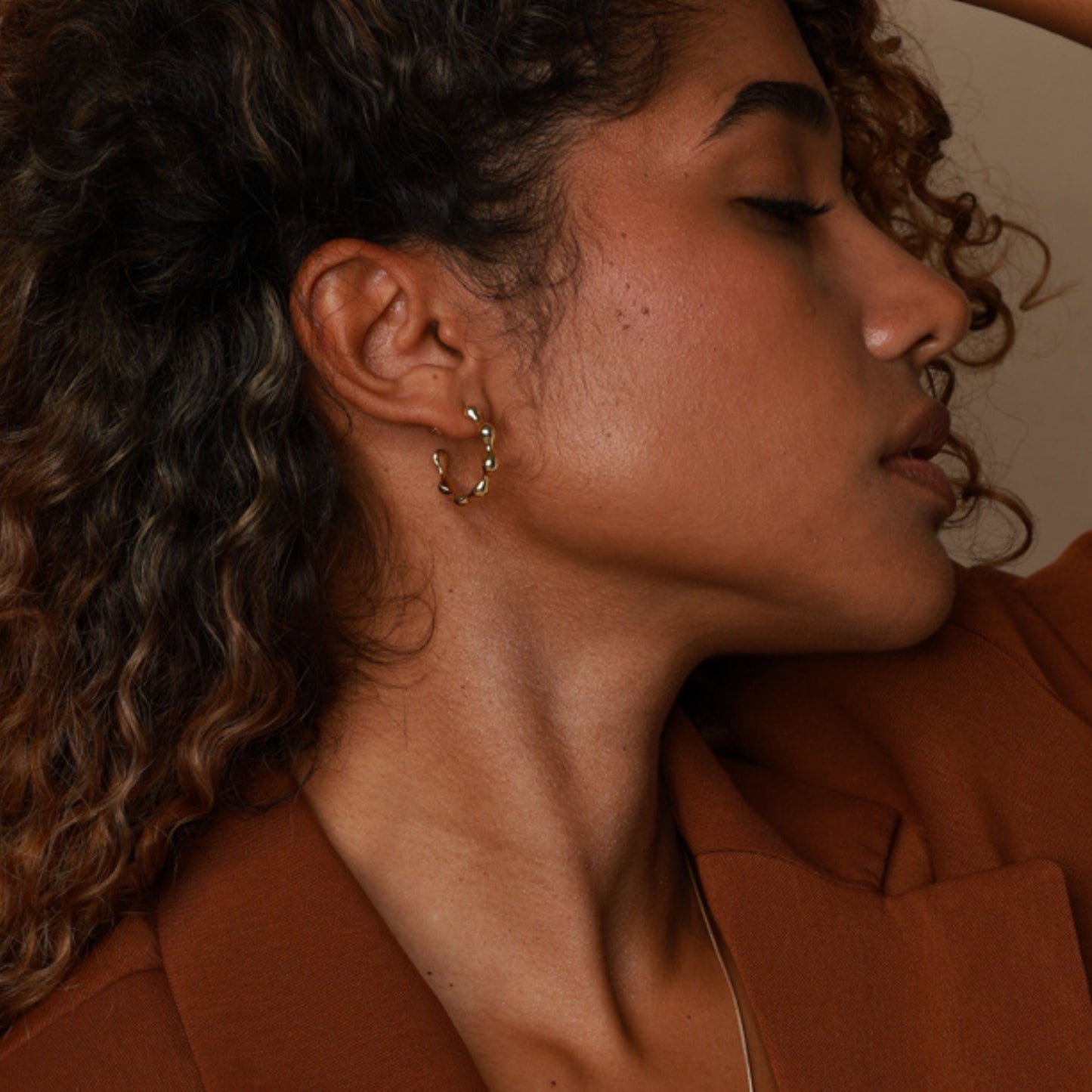 Close-up of a person wearing gold hoop earrings with a warm-toned background