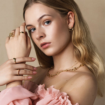 Woman wearing gold jewelry with a pink garment against a beige background