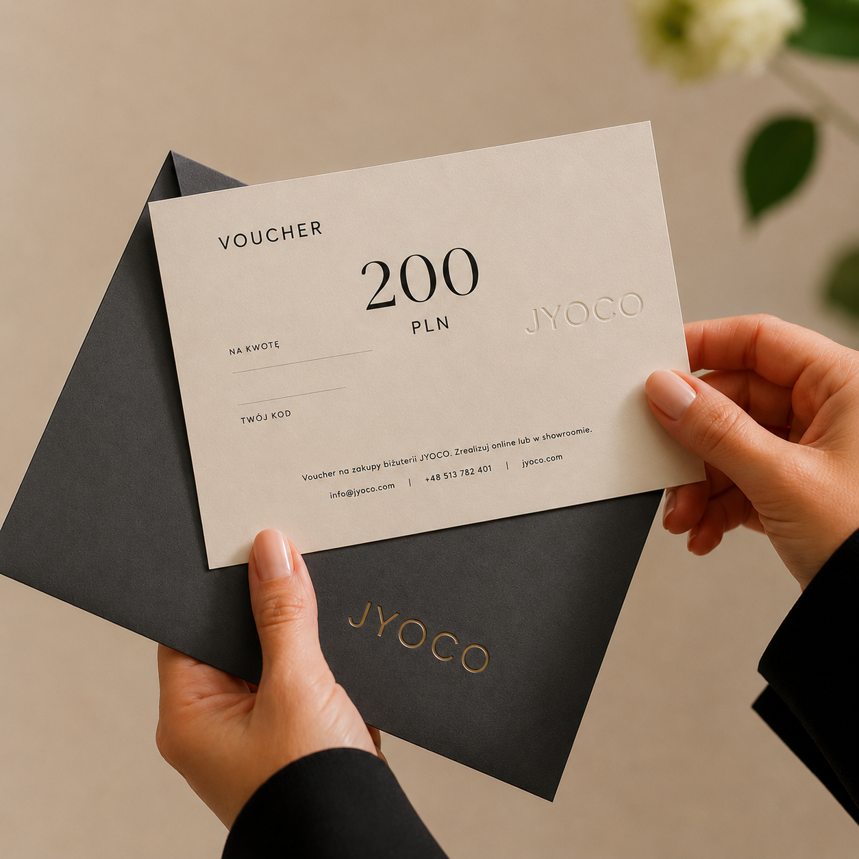 Person holding a JYOCO voucher with a black envelope on a neutral background