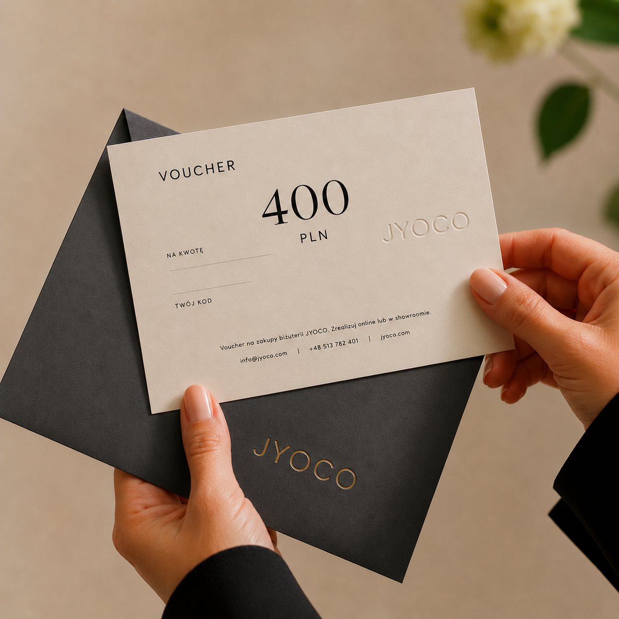 Person holding a JYOCO voucher with a black envelope on a neutral background