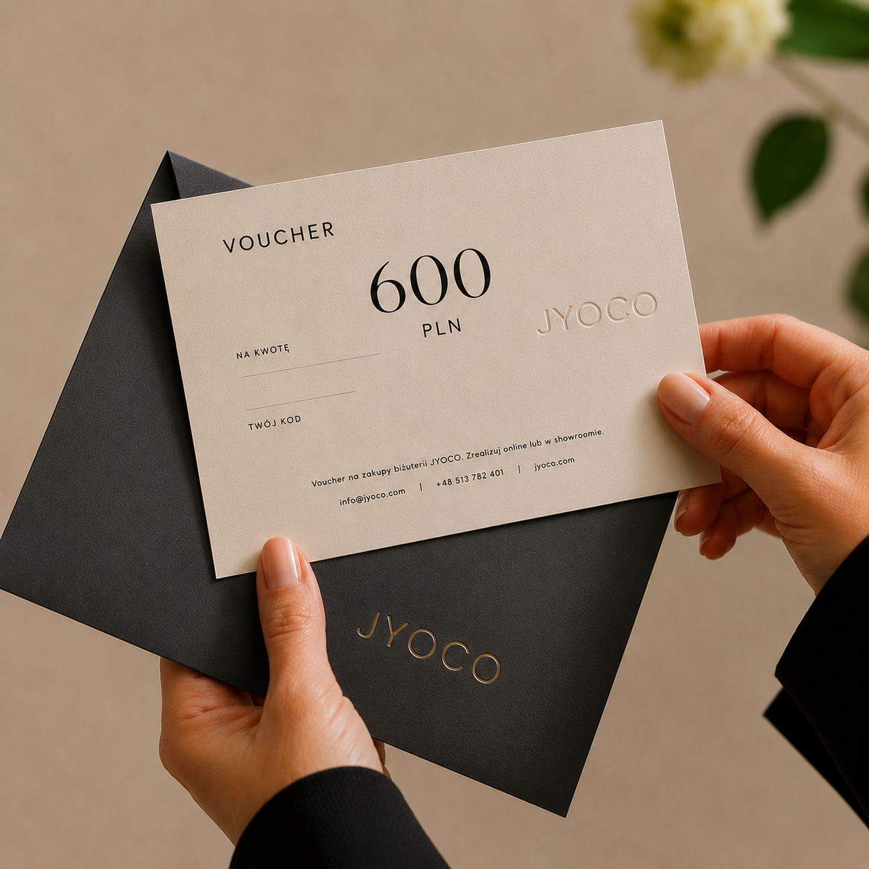 Person holding a JYOCO voucher with a black envelope on a neutral background